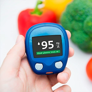 Person holding a home blood sugar monitoring device beside fresh vegetables